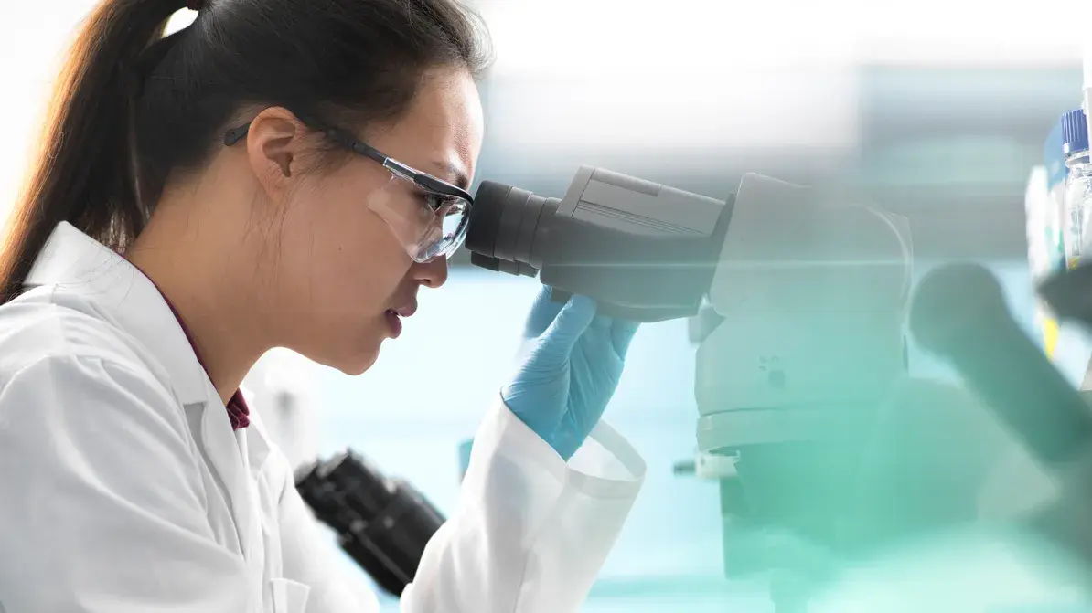 woman peering through a microscope in a laboratory setting