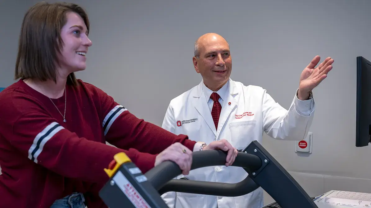 man in a lab coat shows a woman on a treadmill specific data in regards to her trial