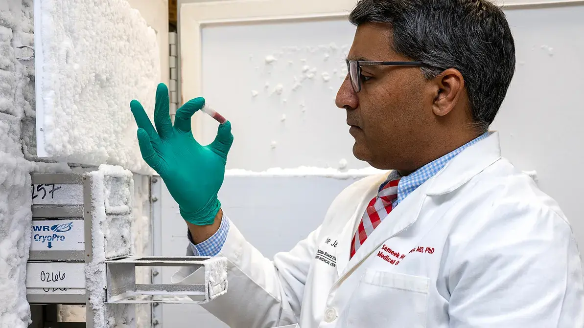 man in a lab coat and rubber cloves holding a frozen blood sample 