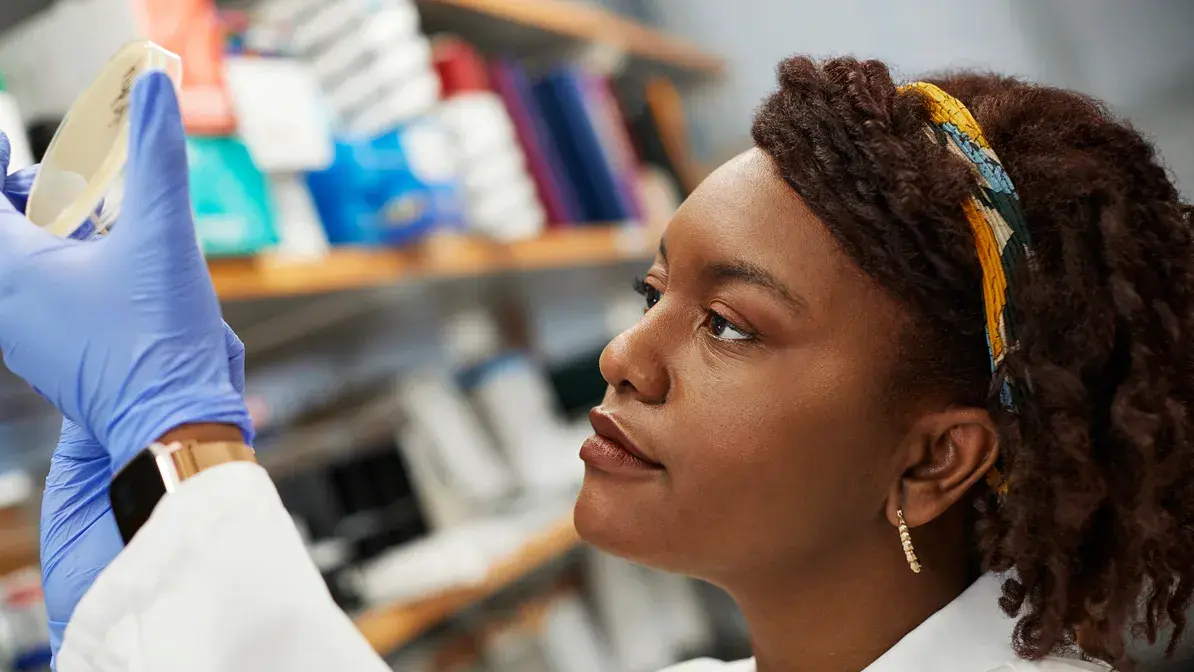 woman wearing a lab coat and latex gloves analyzing a petri dish